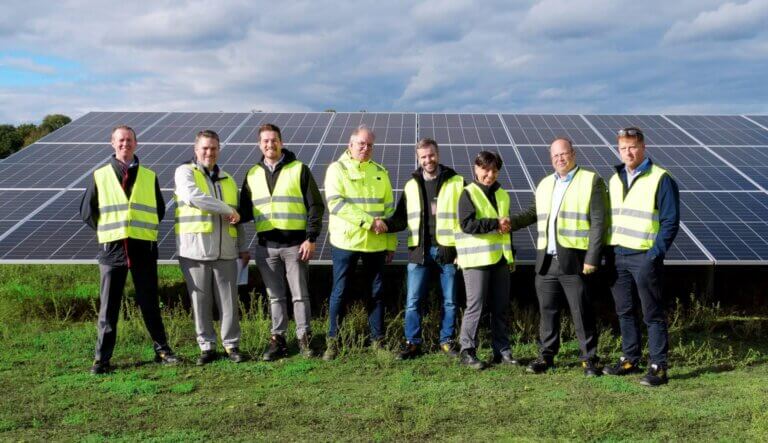 Eight cheerful employees in safety clothing in front of a solar panel