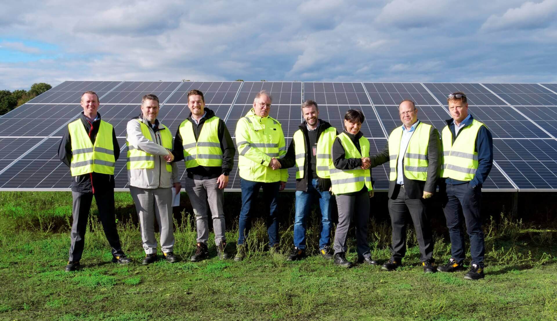 Eight cheerful employees in safety clothing in front of a solar panel
