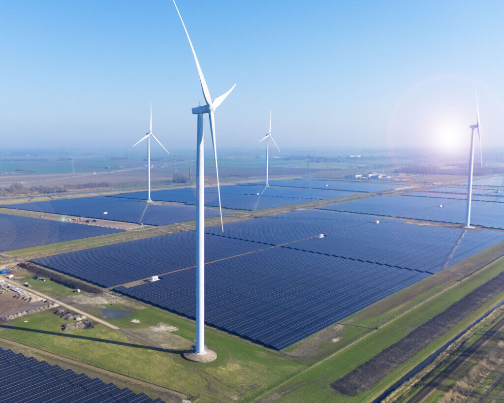 Ein großer Solarpark, der von BELECTRIC gebaut wurde, ist neben Windturbinen aus der Vogelperspektive zu sehen