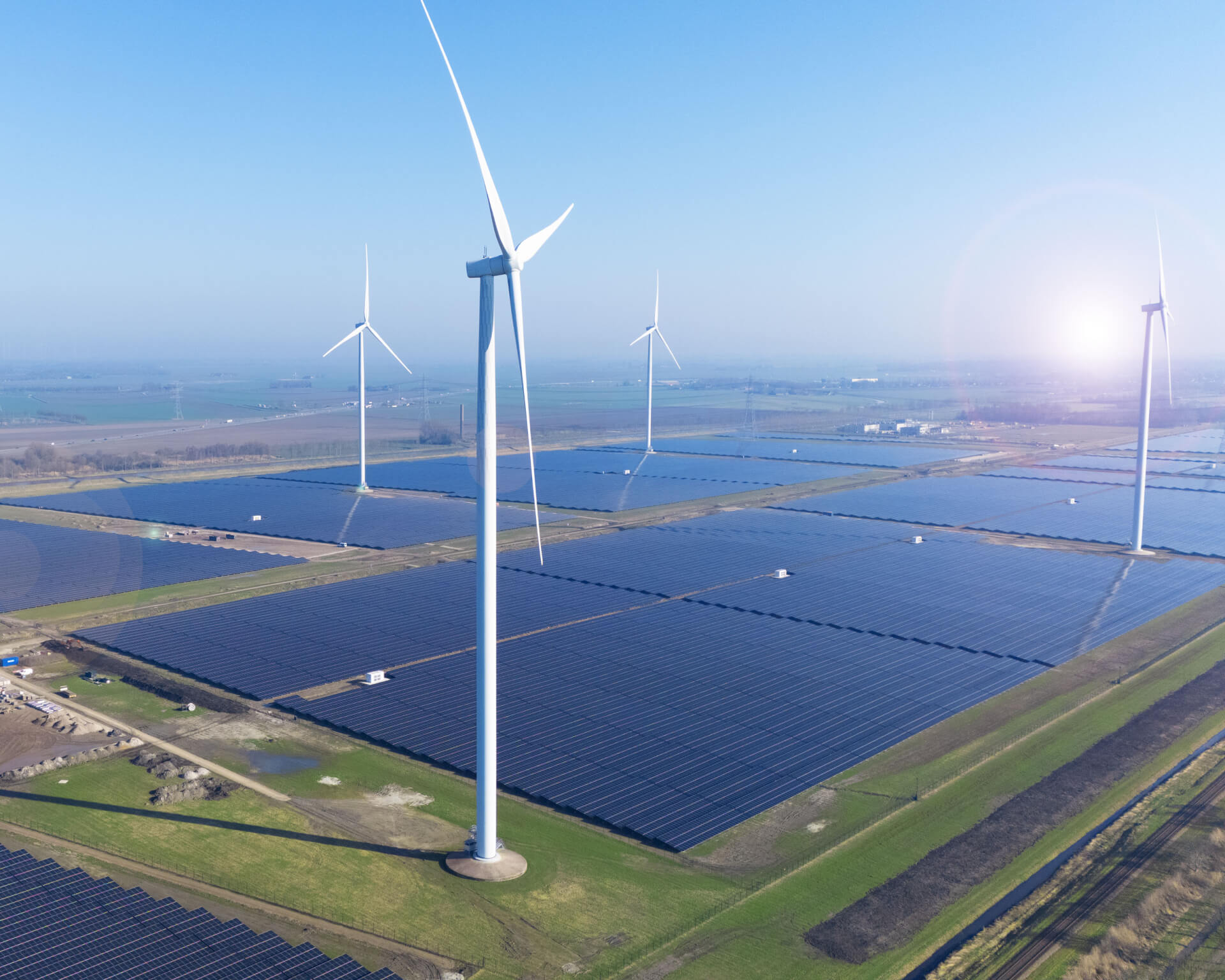 Ein großer Solarpark, der von BELECTRIC gebaut wurde, ist neben Windturbinen aus der Vogelperspektive zu sehen