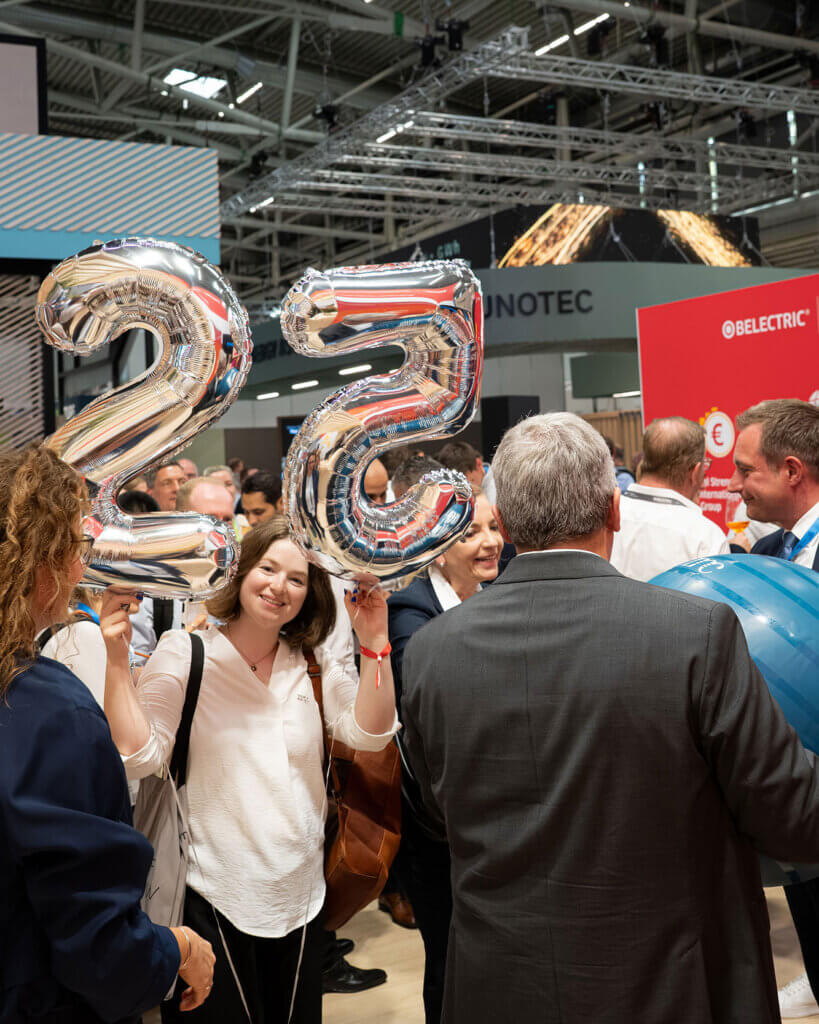 Eine Frau lächelt in die Kamera und hält Luftballons in Form der Zahlen 2 und 5.